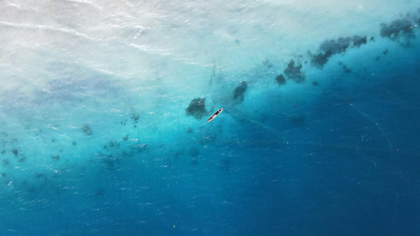 Drone shot of a lone boat in the vibrant blue waters off the coast of Zanzibar, Tanzania.