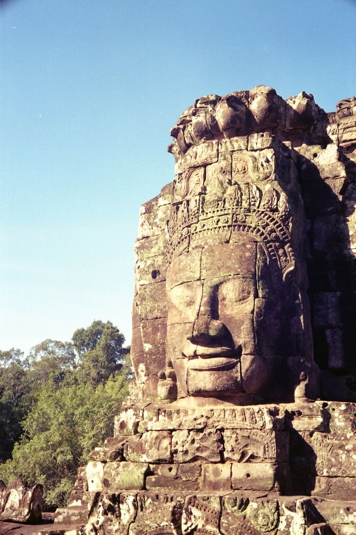 A detailed shot of the iconic stone face at Bayon Temple in Siem Reap, Cambodia under a clear blue sky.